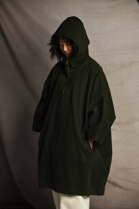 3/4 view of a woman wearing Mónica Cordera poncho in green with the hood. 