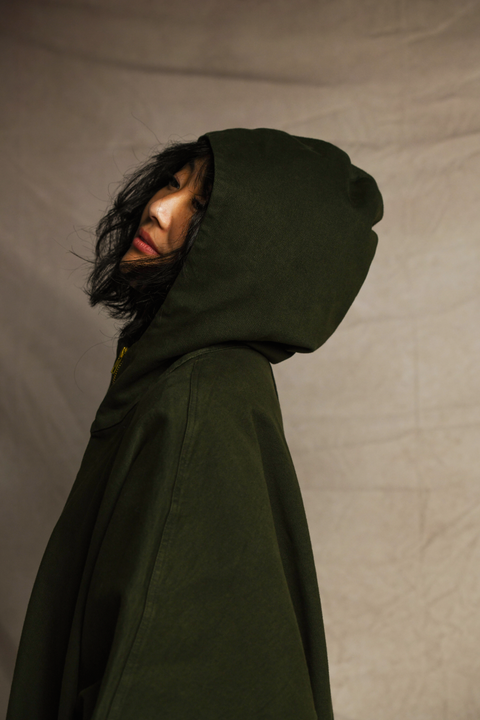 Side view of woman looking into the distance wearing the hood on a Mónica Cordera poncho in green.