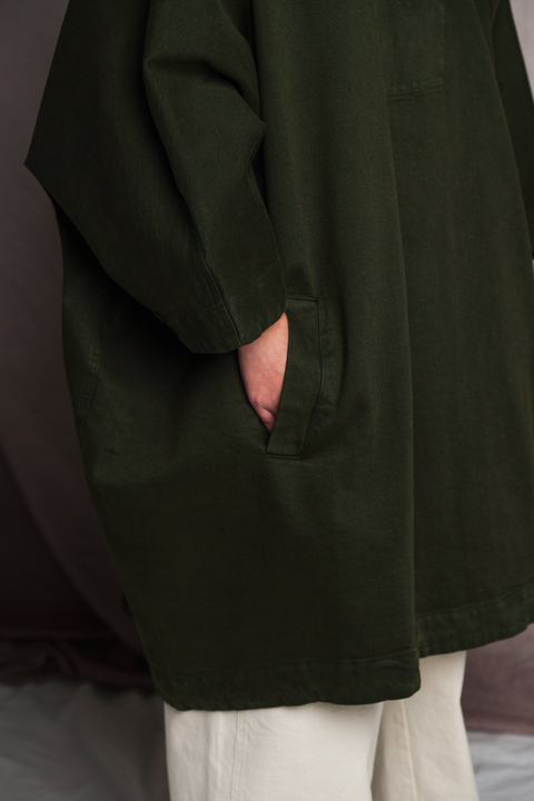 Lower half of person wearing Mónica Cordera poncho in green with their hands in front pockets. 