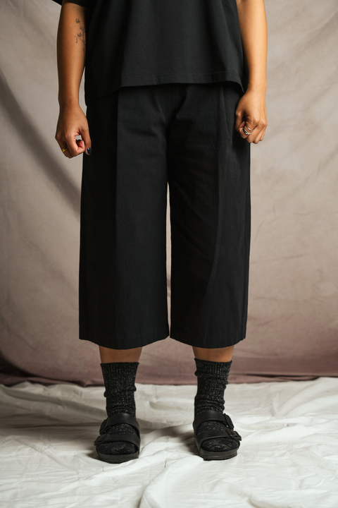 Closer view of 170cm female model standing and wearing bafu osfa half pant in black by The Hinoki. Paired with the Lee t-shirt in black by Studio Nicholson, cotton linen rib socks in black by The Hinoki, and black Birkenstocks